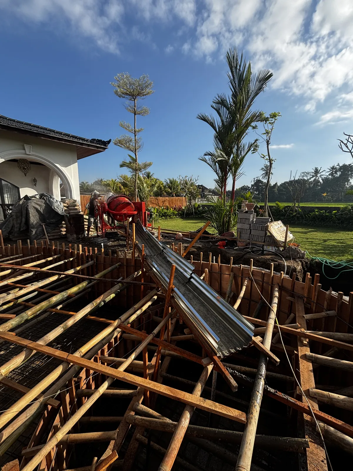 Pour day: a concrete mixer and a steel chute into the pool formwork, the white arched house and the garden behind